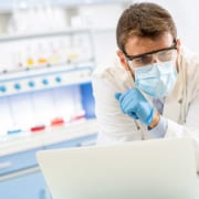 Image of a clinician in PPE using a laptop at work